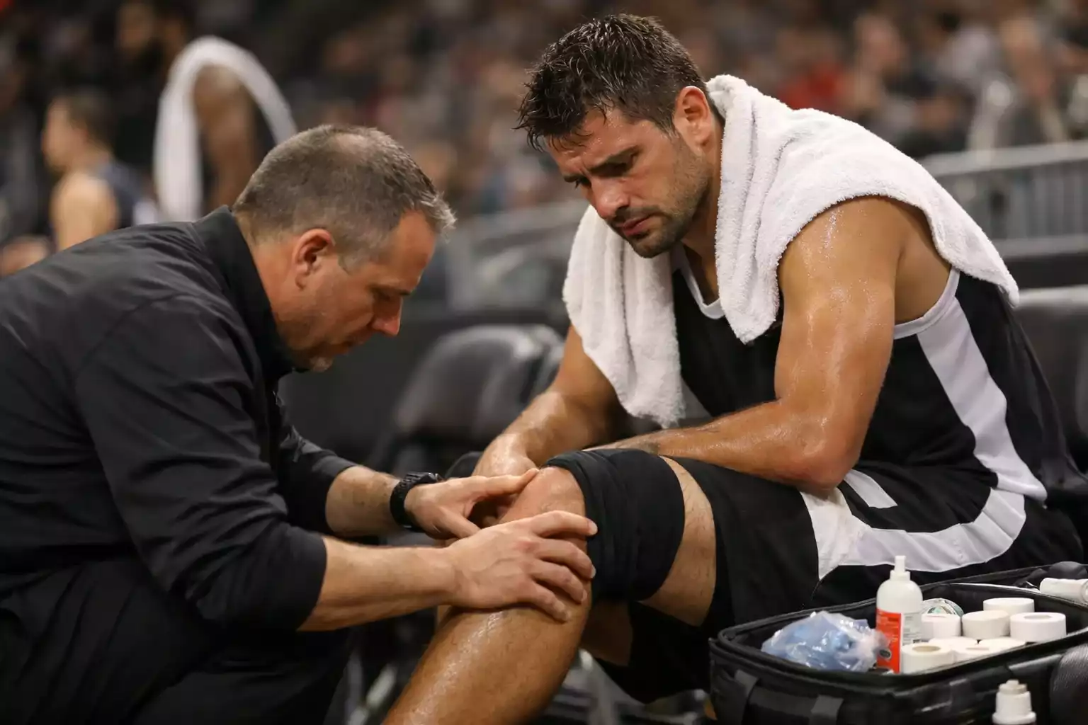 Basketball player with trainer examining injury on bench